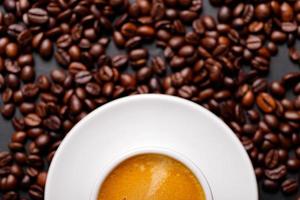 heißer frischer schwarzer kaffee mit milchschaum für morgenmenü in weißer keramiktasse mit gerösteten kaffeebohnen. foto