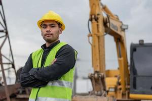 ingenieurmann, der auf der baustelle arbeitet. asiatischer arbeitermann, der auf der baustelle steht und die arme verschränkt. foto