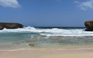 Große Wellen, die an Land auf den weißen Sand von Little Aruba schlagen foto