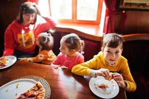 Kinder an Geburtstagen sitzen am Tisch und essen Pizza. foto