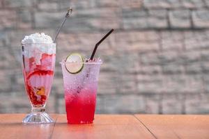 der rote saft, soda rotes wasser-zitronensoda mit zitronenrutsche und erdbeereiscreme mit cremebelag auf holztisch und unscharfem hintergrund foto