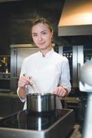 Porträt einer selbstbewussten und lächelnden jungen Köchin in weißer Uniform, professionelle Küche im Hintergrund foto