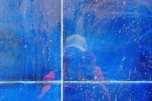 Reflexion einer Person mit einer Fotokamera in der Wand der blauen flüssigen Keramikfliesen, im abstrakten Hintergrund, in der Schmutzbeschaffenheit und im Muster. foto