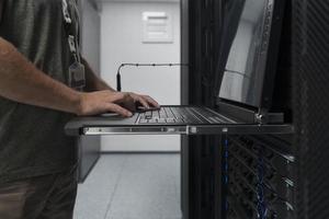 Nahaufnahme der Hände eines Rechenzentrumsingenieurs mit Tastatur auf einer spezialisierten Einrichtung eines Supercomputer-Serverraums mit männlichem Systemadministrator, der mit einem Datenschutznetzwerk für Cybersicherheit arbeitet. foto