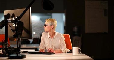 Frau, die im dunklen Büro am Computer arbeitet foto