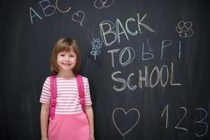 Schulmädchen mit Rucksack, der Tafel schreibt foto