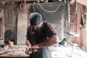 Löffelmeister in seiner Werkstatt mit Holzprodukten und Werkzeugen foto