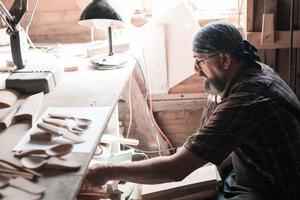 Löffelmeister in seiner Werkstatt mit Holzprodukten und Werkzeugen, die das richtige Holz für die Herstellung von Küchengeschirr aus Holz auswählen. foto