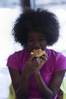 Frau mit Afro-Frisur, die leckere Pizzastücke isst foto