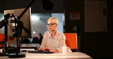 Frau, die im dunklen Büro am Computer arbeitet foto