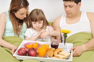 Glückliche junge Familie frühstückt im Bett foto