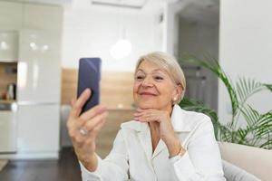 oma macht selfies zu hause im wohnzimmer. Nahaufnahme Porträt einer fröhlichen, entzückenden, charmanten, schönen älteren Dame, Oma, Oma, die ein Selfie macht. alters-, ruhestands- und personenkonzept