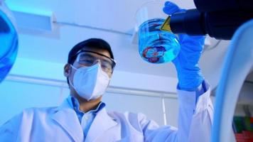 asiatischer wissenschaftler, der recherchiert und eine flüssigkeit in einem testkolben im labor überprüft. foto
