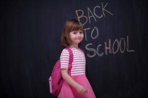 Schulmädchen mit Rucksack, der Tafel schreibt foto