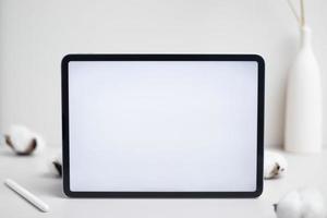 leerer weißer bildschirm der tablette mit bleistift und baumwollblume auf weißem hintergrundmodell für design foto