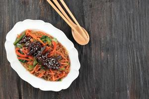 Japchae, gebratene Glasnudeln mit Gemüse und Rindfleisch, serviert auf einem weißen Teller. koreanische authentische küche foto