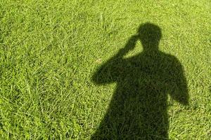 Schatten einer Person, die ein Telefon auf dem Gras benutzt foto