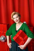 Reife stilvolle elegante Frau mit Geschenkbox auf rotem Hintergrund. party, mode, feier, anti-age-konzept.