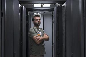 Porträt eines männlichen Technikers oder Netzwerkadministrators, der tapfer als Held mit verschränkten Armen im Serverraum des Rechenzentrums steht. foto