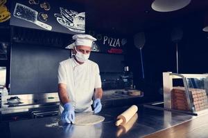 koch mit schützender coronavirus-gesichtsmaske, die pizza zubereitet foto