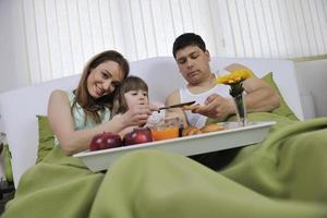 Glückliche junge Familie frühstückt im Bett foto