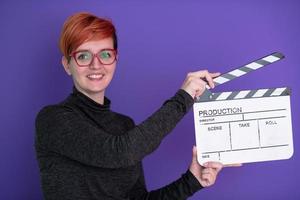 Rothaarige Frau mit Filmklöppel auf violettem Hintergrund foto