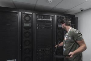 Rechenzentrumsingenieur, der die Tastatur in einer spezialisierten Einrichtung eines Supercomputer-Serverraums mit männlichem Systemadministrator verwendet foto