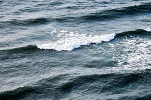 tiefblaues meerwasser, das mit schaumigen wellen spritzt, dunkelblaue gewellte ozeanwasseroberfläche, stürmisches meer foto