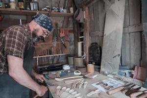 Löffelmeister in seiner Werkstatt mit Holzprodukten und Werkzeugen foto