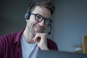 fröhlicher mann deutschsprachiger callcenter-berater im headset mit mikrofon arbeitet von zu hause aus foto