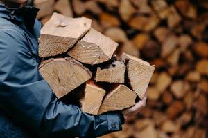 nicht erkennbarer mann trägt einen holzhaufen, um feuer in jacke zu machen. gesichtsloser Mann trägt Brennholz ins Haus foto