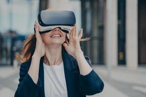 Erstaunte rothaarige Büroangestellte, die beim Ausprobieren einer VR-Brille im Freien aufgeregt ist foto