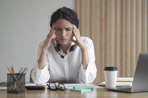 gestresste Unternehmerin, die unter Kopfschmerzen leidet und Schläfen massiert, während sie zu Hause im Büro sitzt foto