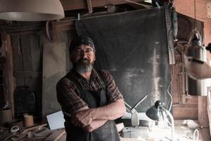 Löffelhandwerksmeister in seiner Werkstatt mit handgefertigten Holzprodukten und Werkzeugen foto