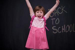 Schulmädchen mit Rucksack, der Tafel schreibt foto