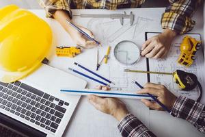 Zwei Kollegen diskutieren über Datenverarbeitung und Tablet, Laptop mit einem Architekturprojekt auf der Baustelle am Schreibtisch im Büro foto