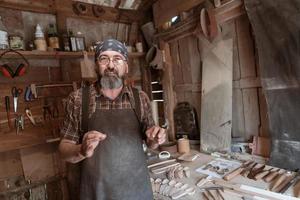 Löffelmeister in seiner Werkstatt mit Holzprodukten und Werkzeugen foto