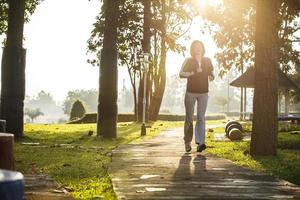 asiatische frau, die im park mit bewölktem himmel und linseneffekt joggt foto