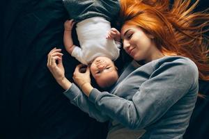 glückliche Mutter mit Baby, die zusammen auf dem Bett liegt foto