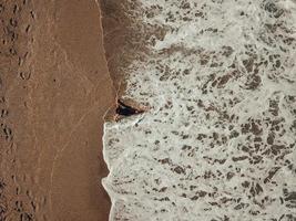 Luftdraufsicht junge Frau, die auf dem Sandstrand und den Wellen liegt foto