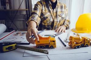 Zwei Kollegen diskutieren über Datenverarbeitung und Tablet, Laptop mit einem Architekturprojekt auf der Baustelle am Schreibtisch im Büro foto