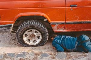 Mann liegt unter einem 4x4-Auto auf einer unbefestigten Straße foto