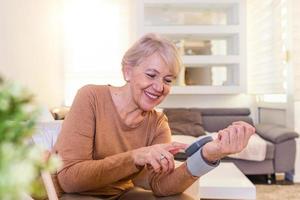 Reife Frau, die den Blutdruck überprüft. Nahaufnahme eines Blutdruckmessgeräts zur Hand. digitales Tonometer auf der menschlichen Hand. Porträt einer älteren Frau, die ihren Blutdruck misst foto