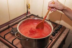 eine frau bereitet frischen gesunden saft aus tomaten zu. Frisch zubereiteter Tomatensaft wird in einem Topf gekocht und für die Langzeitlagerung konserviert. diätkonzept für einen gesunden lebensstil. foto