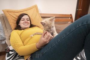 schöne junge hispanische Frau, die auf ihrem Bett liegt und mit ihrem kleinen Kätzchen spielt foto