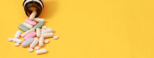 Tablettenfläschchen verschüttet. bunte Pillen auf Oberflächentabletten auf gelbem Hintergrund. Ansicht von oben. drogenmedizinisches gesundheitskonzept foto
