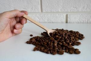 Die Hand hält einen kleinen Holzlöffel mit Kaffeebohnen für die Herstellung von köstlichem Kaffee. ganze geröstete Kaffeebohnen zum Mahlen foto