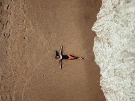 Luftdraufsicht junge Frau, die auf dem Sandstrand und den Wellen liegt foto