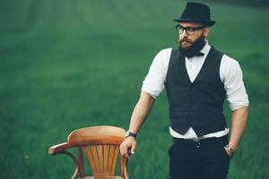 Mann mit Bart, der auf dem Feld in der Nähe des Stuhls denkt foto