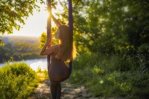 Eine junge Turnerin macht Aerial Yoga in der Natur des Parks mit einer Kombination aus traditionellen Yoga-Posen, Pilates und sanftem Tanz foto